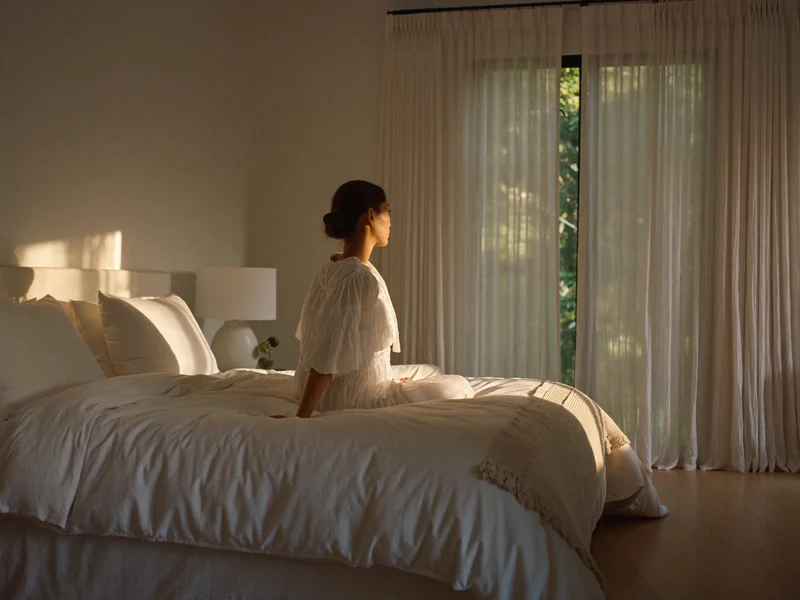 Ruhiges Schlafzimmer im Morgenlicht mit Leinenbettwäsche, Überwurf und Vorhängen